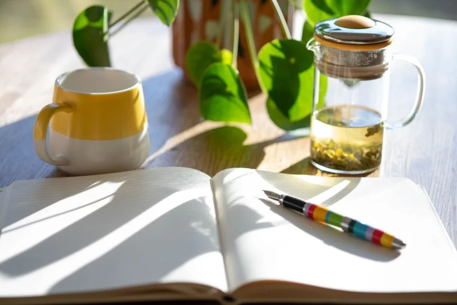 Bureau ensoleillé avec un carnet, un stylo, une tasse et une infusion près d’une plante